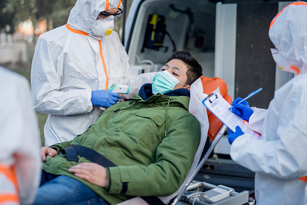 People with protective suits helping man outdoors on stretcher