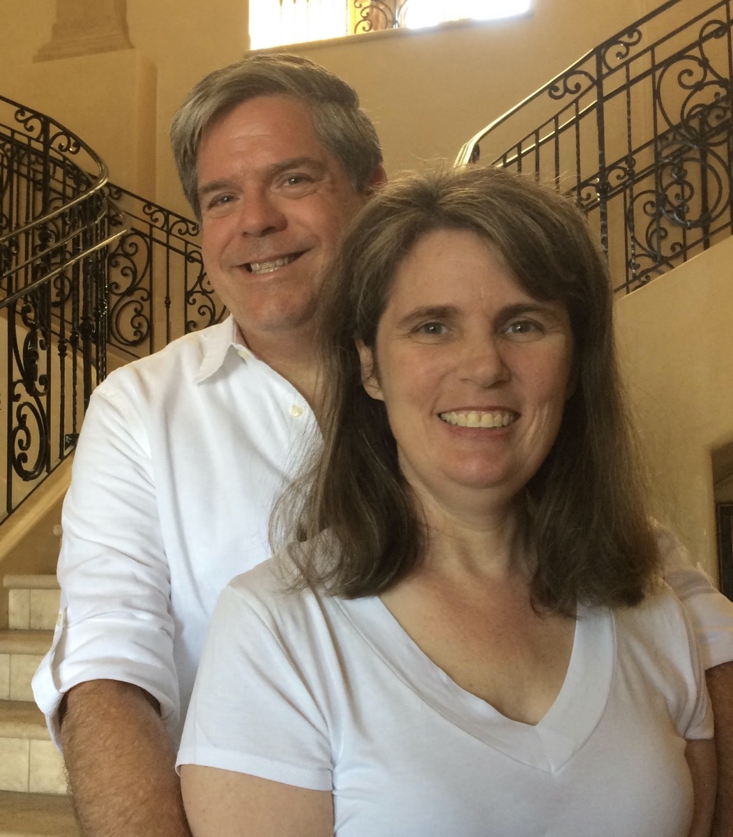 a man in a white button up shirt stands behind his wife hugging her.