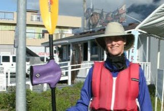 a woman in a long blue water resistant coat and a red life jacket holds a kayak paddle