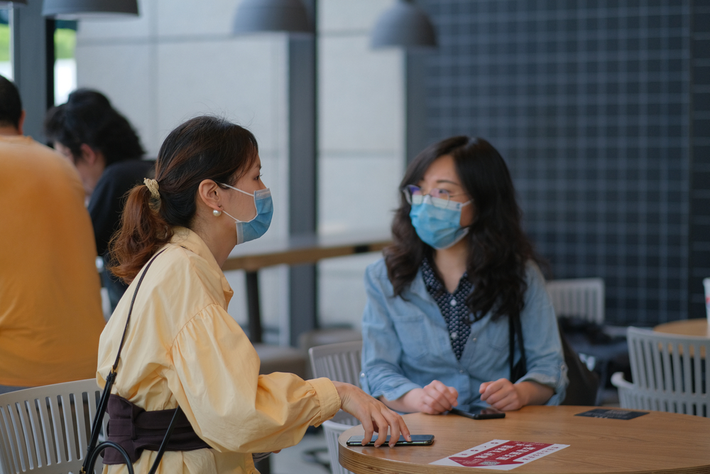 young women talking in cafe, wearing surgical mask to prevent infection of coronavirus