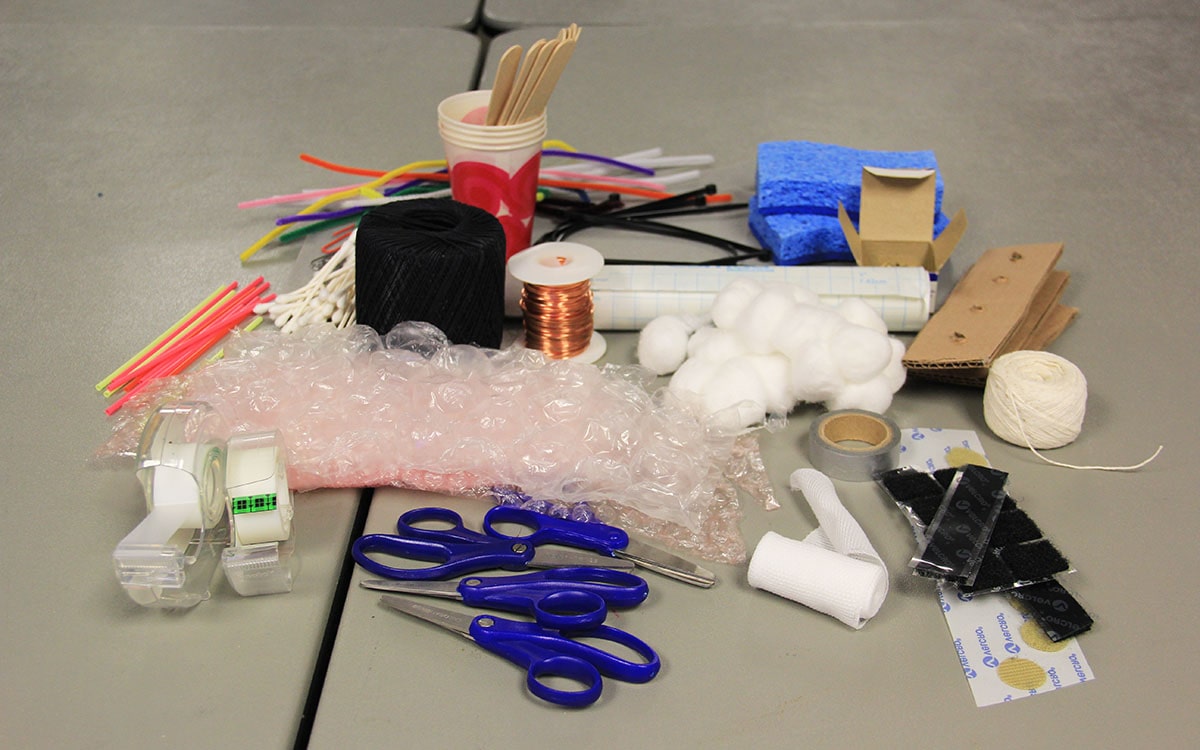 Pile of glove building materials, including scissors, tape, bubble wrap, cardboard, and cotton balls.