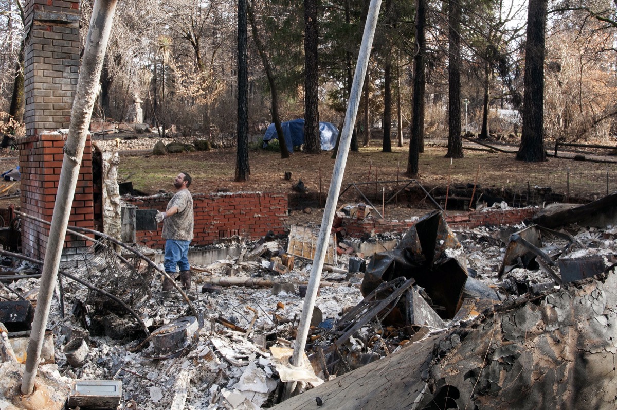 a man stand amid rubble of a scorched house