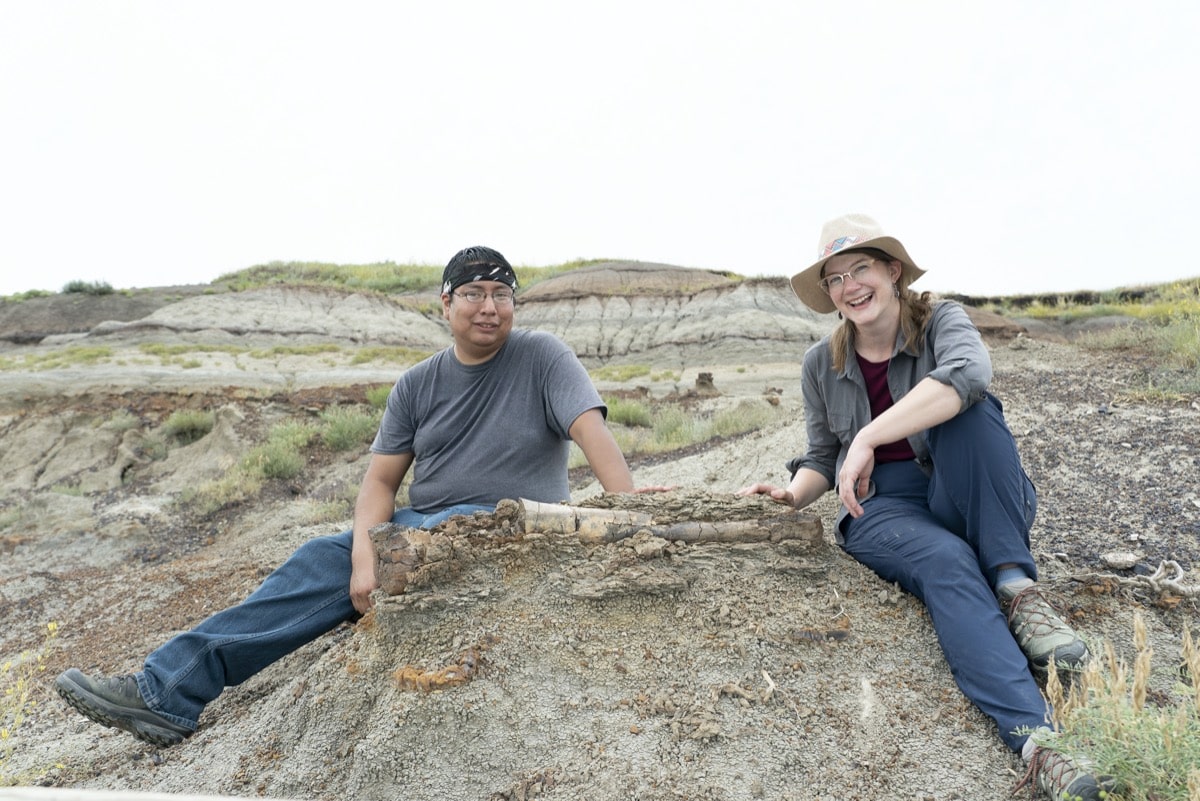 a woman and a man sit next to a fossil still embedded in the ground