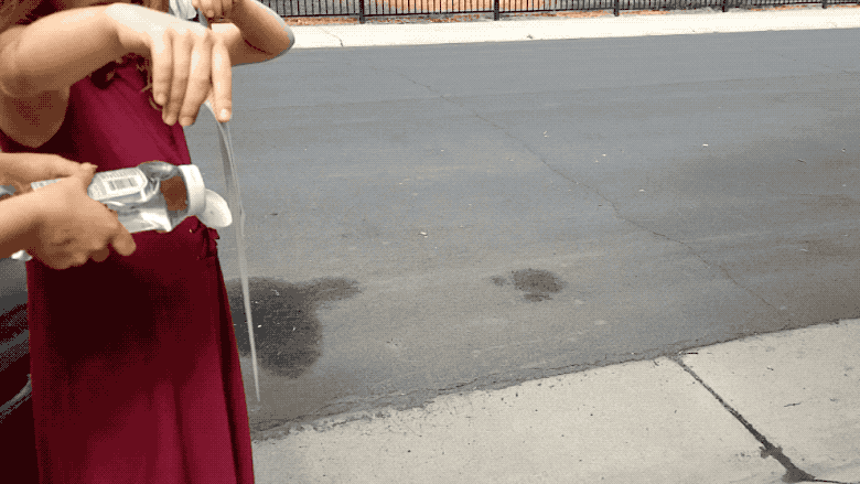 Two people squirt water with a ketchup bottle through a placemat to spray water on dry pavement