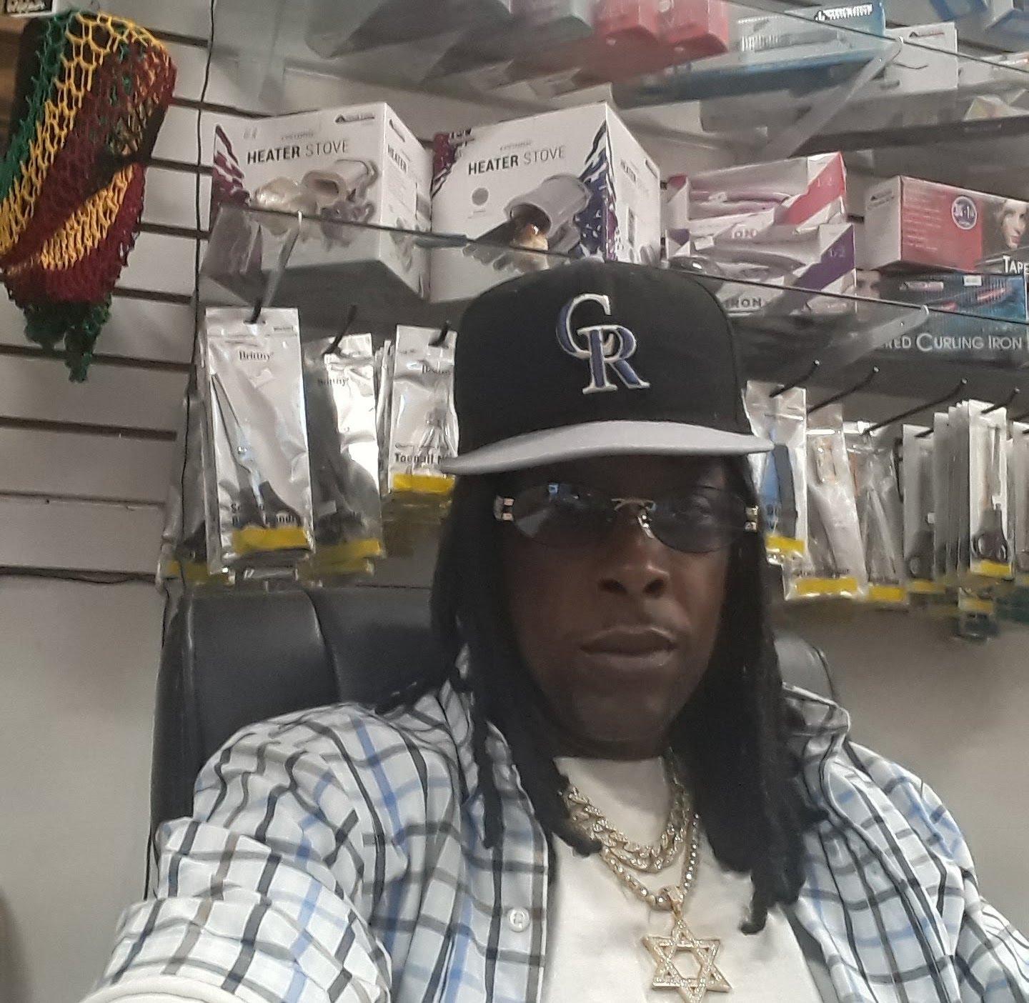 a black man wearing sunglasses, a baseball cap, and a plaid shirt in a store. 