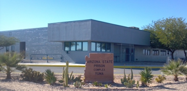 a gray building with a sign in the shape of the state of arizona that reads "arizona state prison complex yuma"