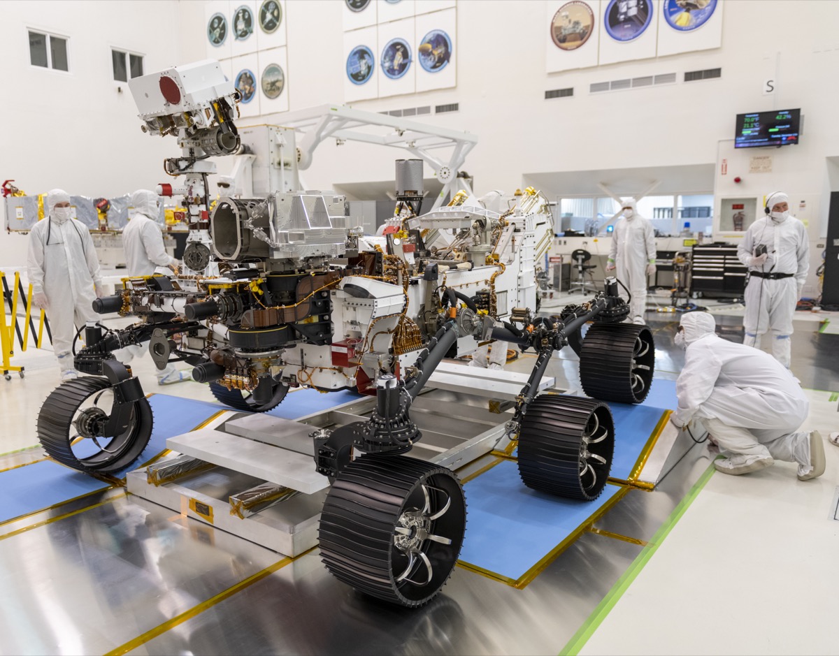 a golf cart sized robot rover with six wheels in a laboratory. researchers in white hazmat suits work on the rover