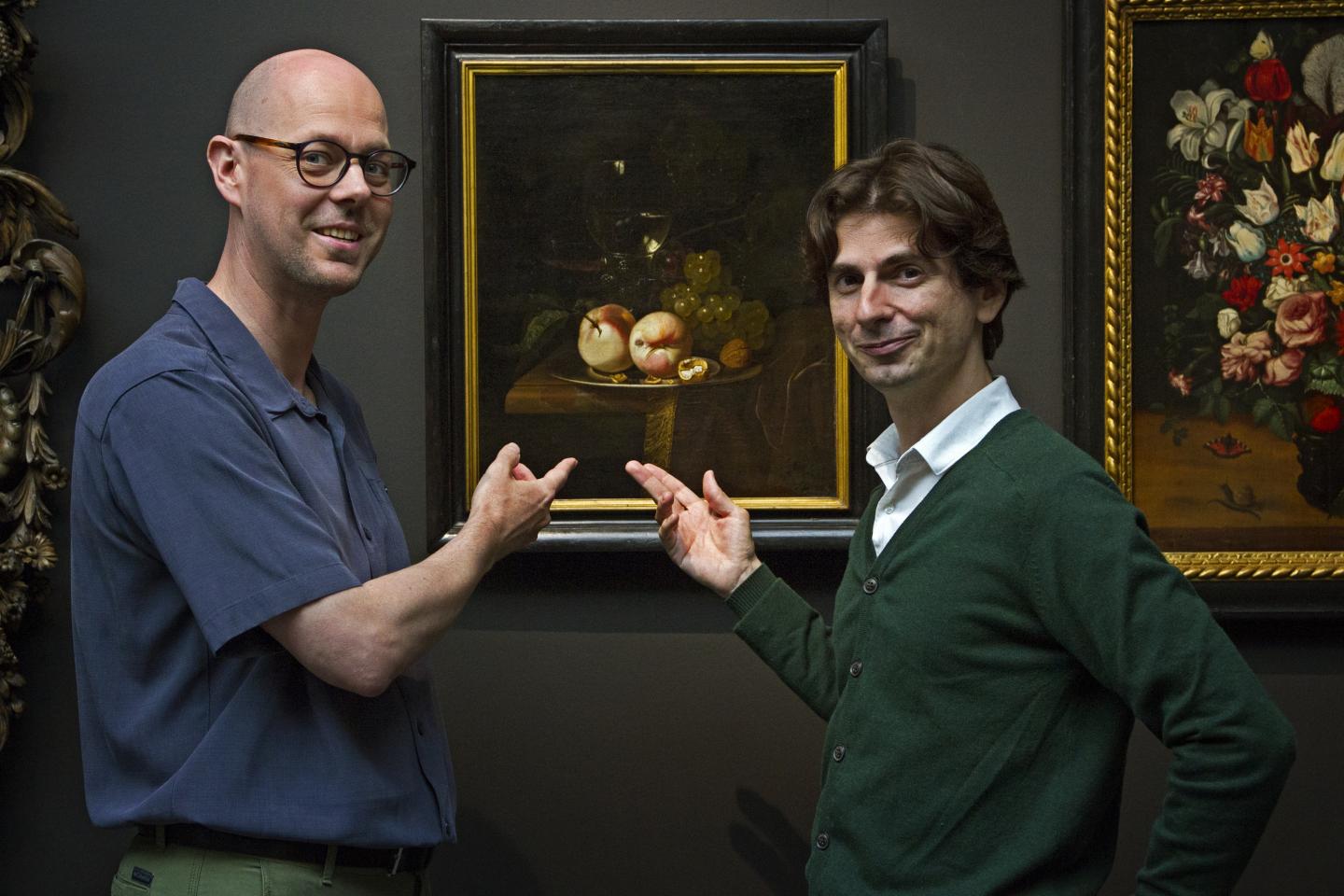 two men standing in front of oil painting in museum