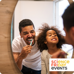 a father and 5-year-old daughter looking into a mirror; the father is brushing his teeth and smiling, and the daughter is smiling large