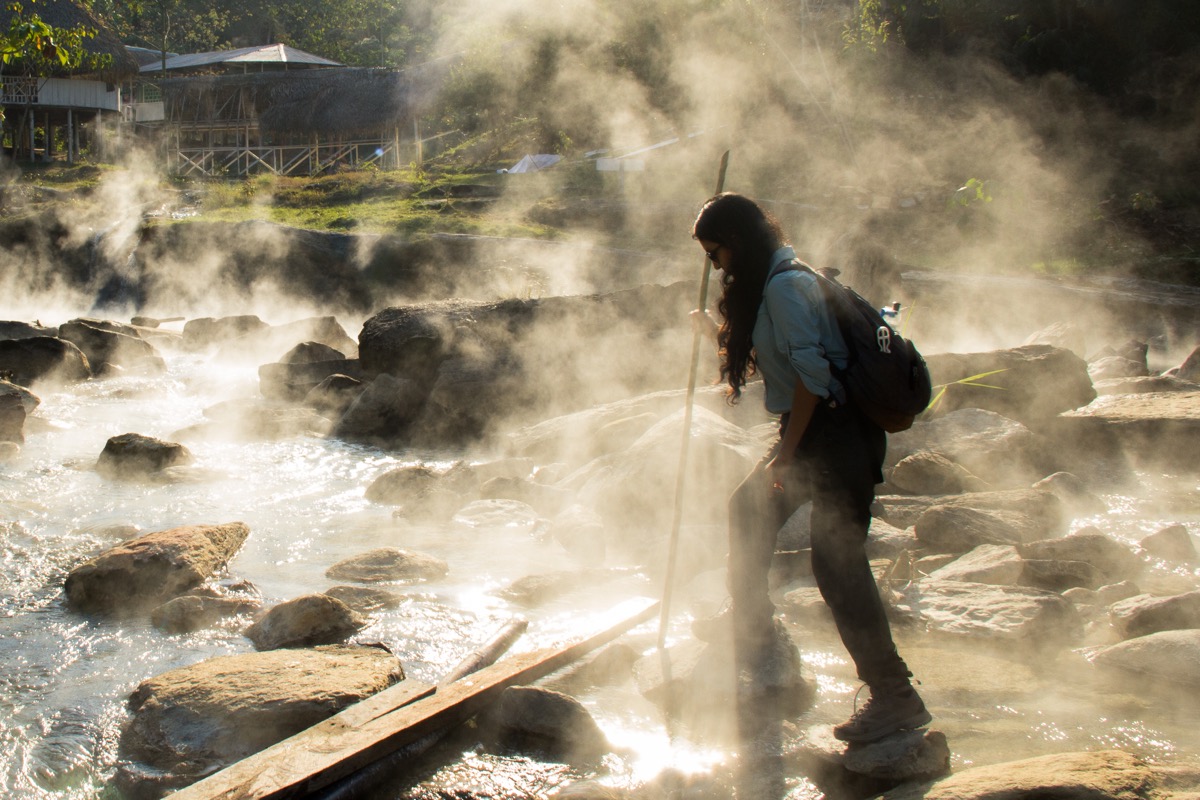 a woman scientist walks across river rocks with steam surrounding her