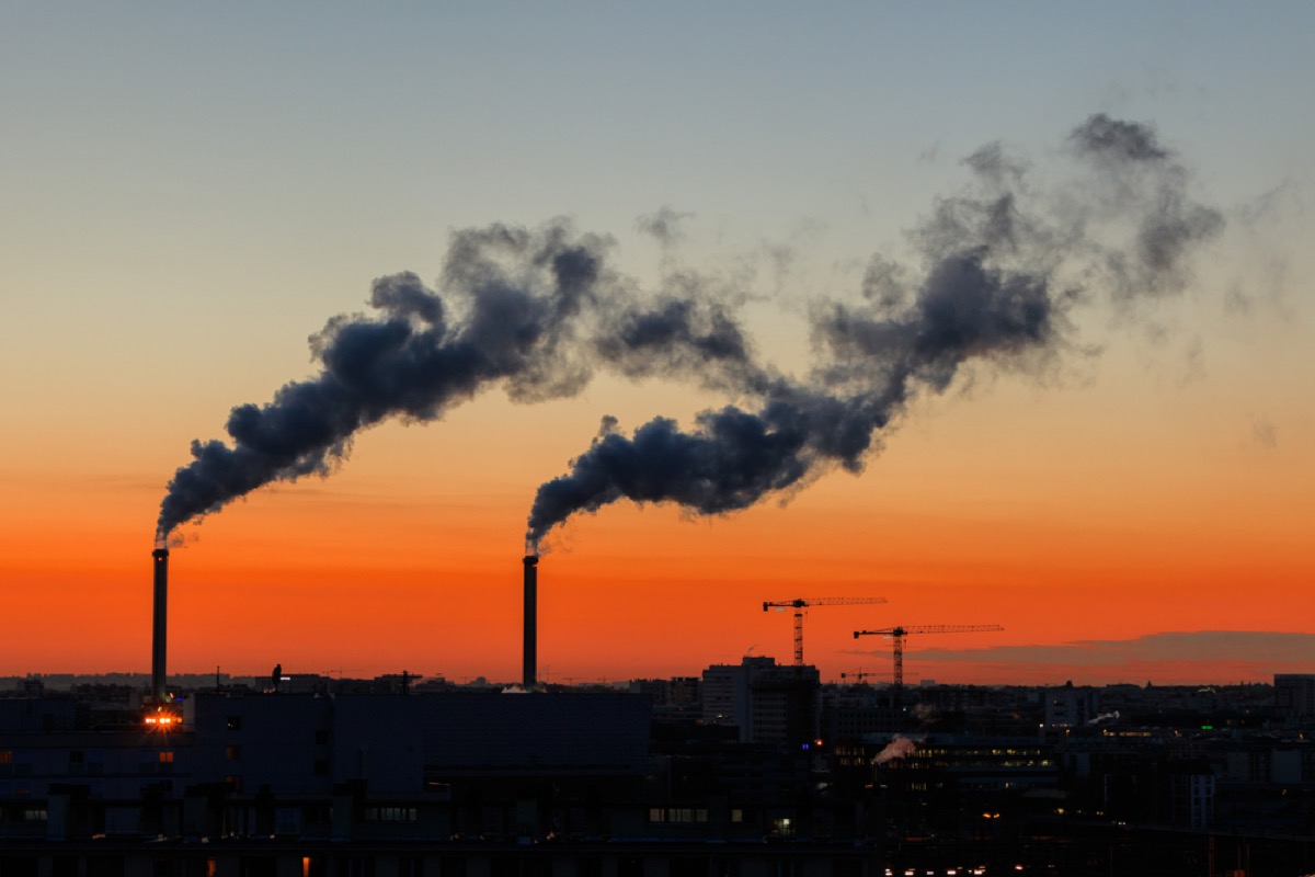 smoke stacks emitting pollution into the air, shadowed by an orange sunset