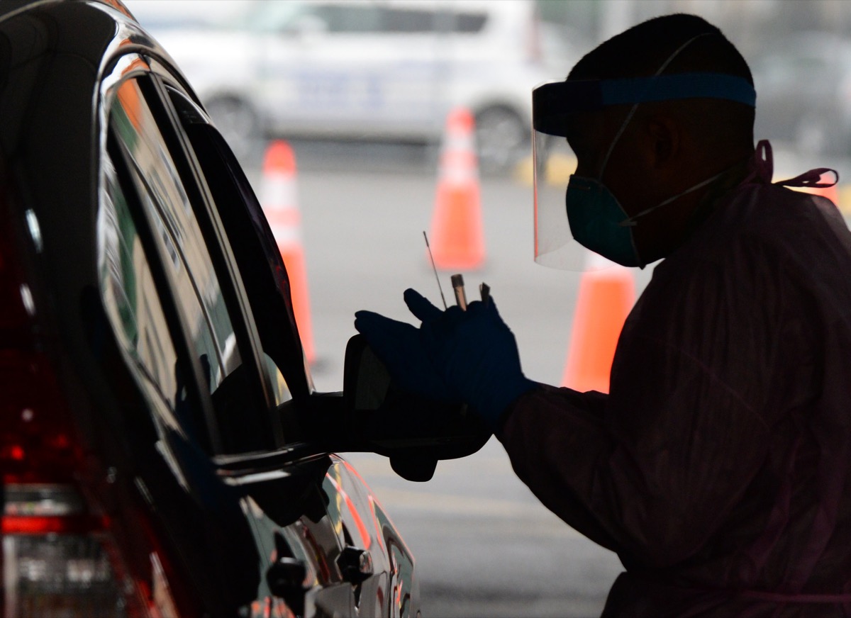 a medic holding a swab and test tube next to a car in the shadows