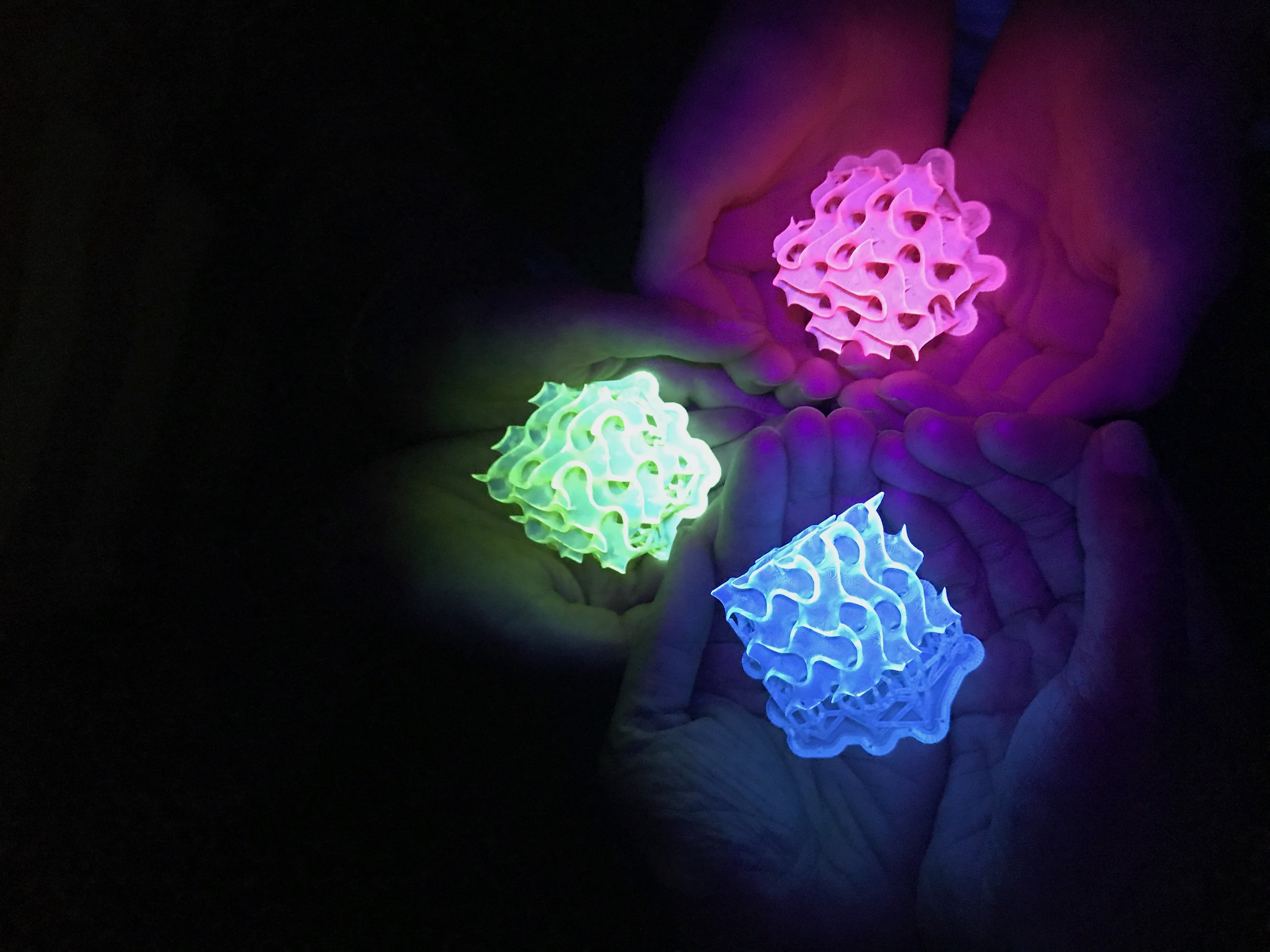 three pairs of hands holding Glowing 3D-printed gyroids