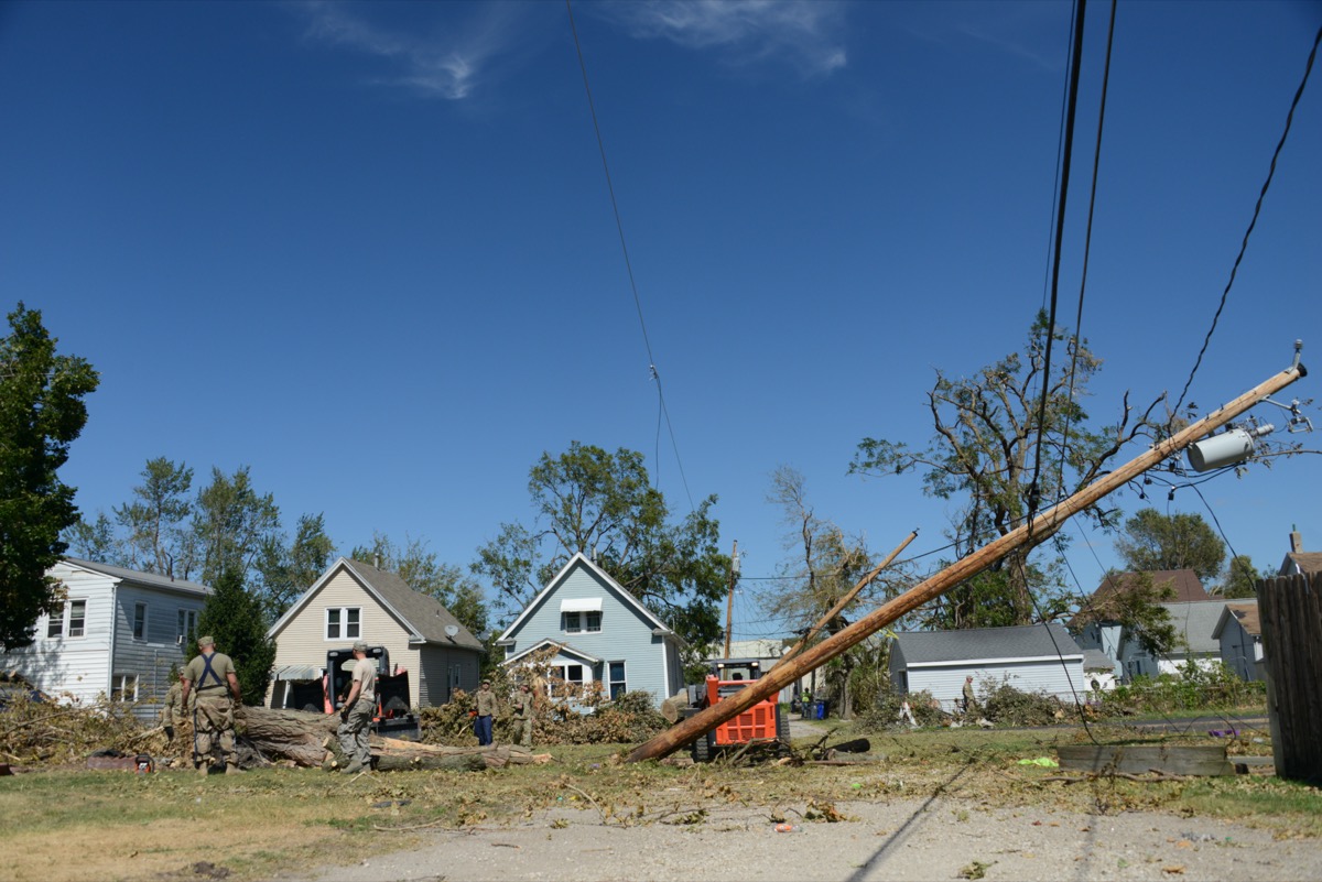 a bunch of downed trees and power lines in front of a row of houses.