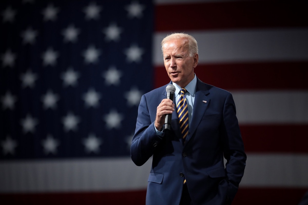 a man in a suit speaking into a microphone, standing in front of an american flag