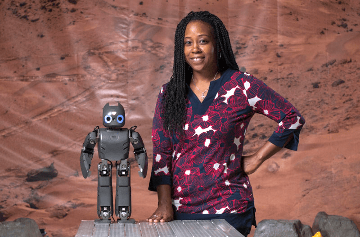 a black woman standing next to a small humanoid robot