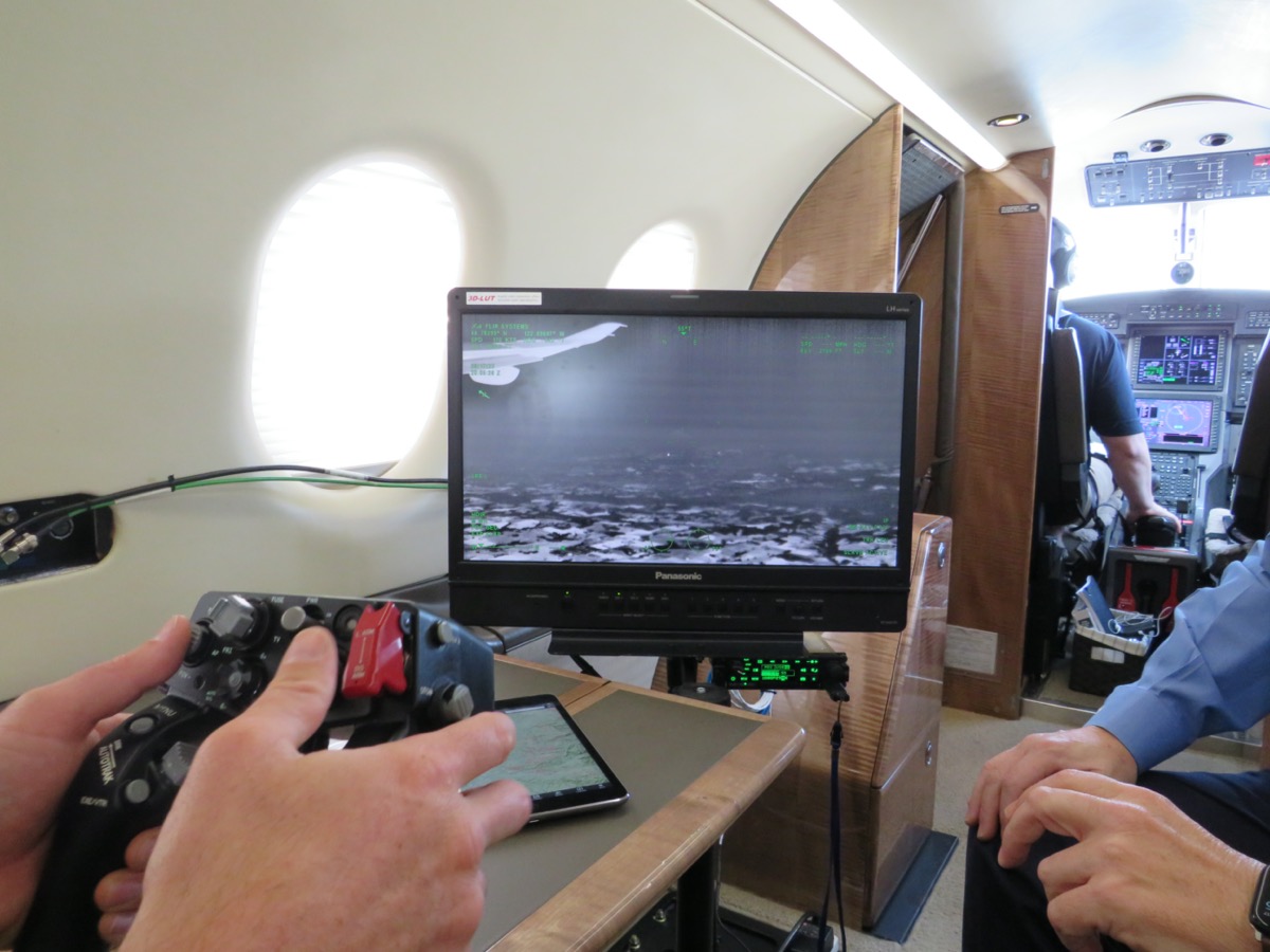 a person uses a video game-like controller to maneuver a camera's view on a computer screen. the person is doing it from inside the cabin of a plane