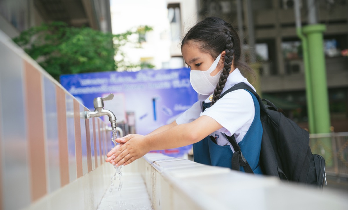 an asian student washing hands at an outdoor wash basin in a school wearing a face mask