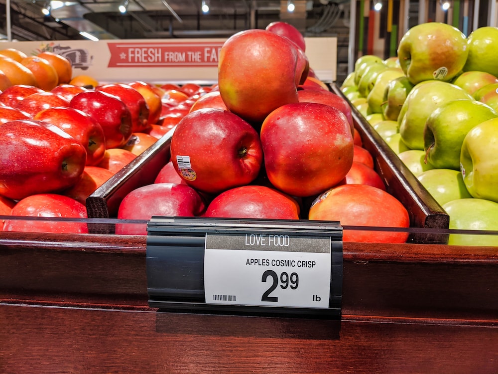 shiny reddish-pink apples stacked in a pyramid in a grocery store with a tag for price of $2.99