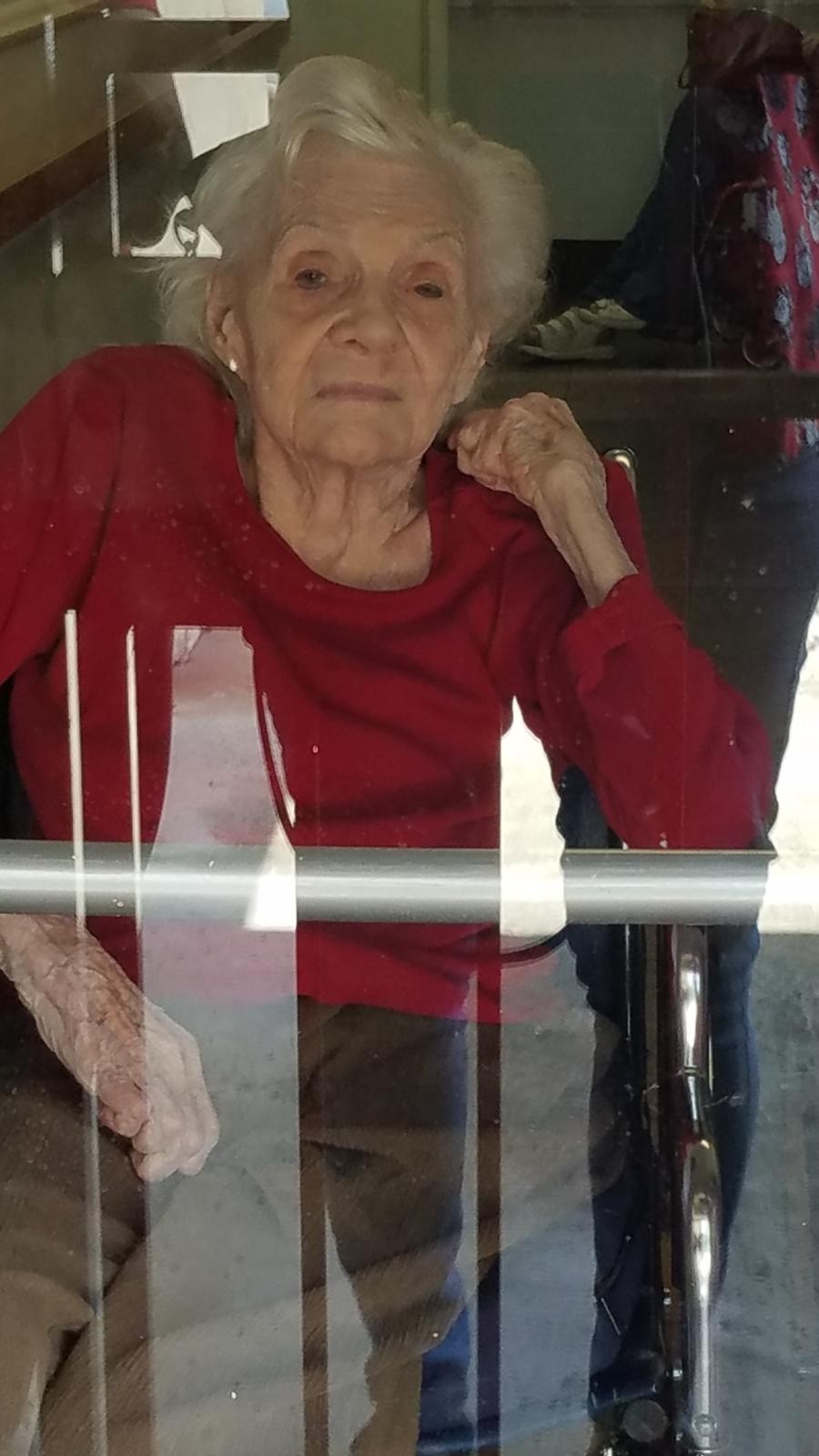 an image of an older woman in a red sweater - seen through a window