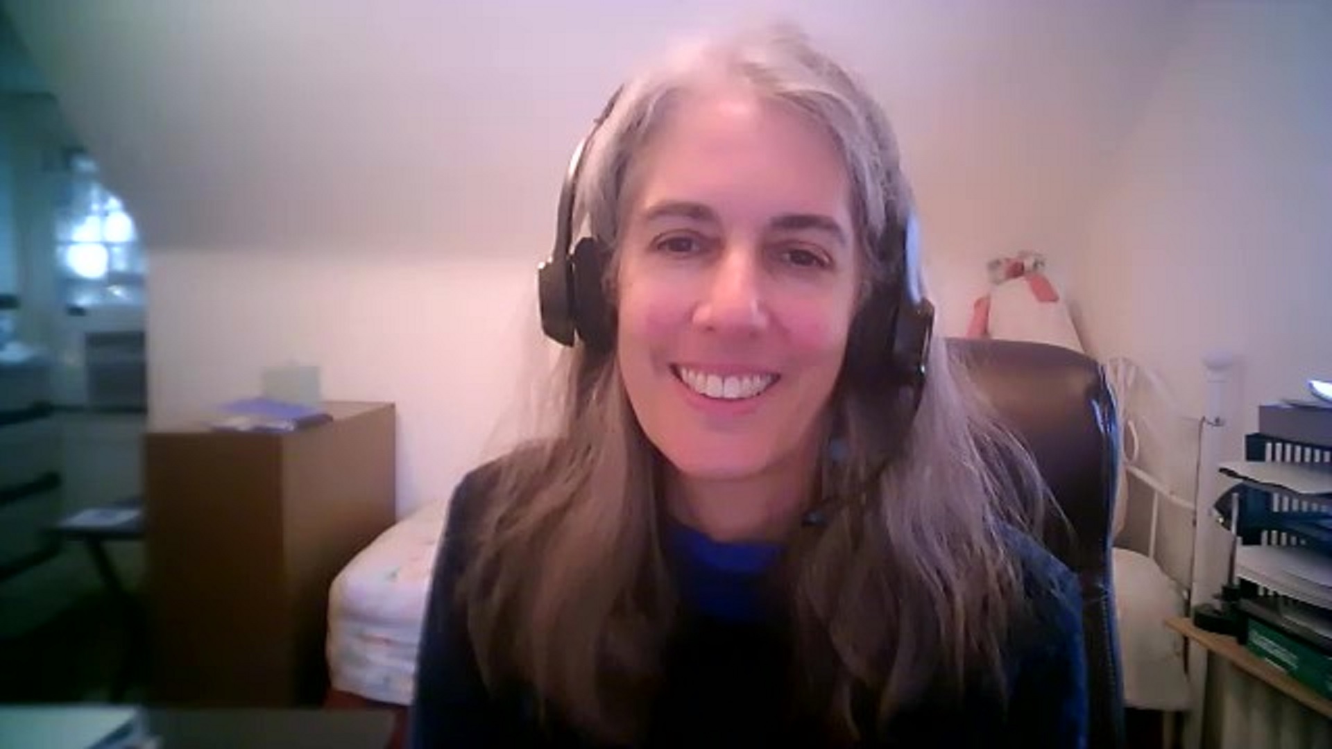 a screenshot from a video chat of a White woman smiling wearing a headset