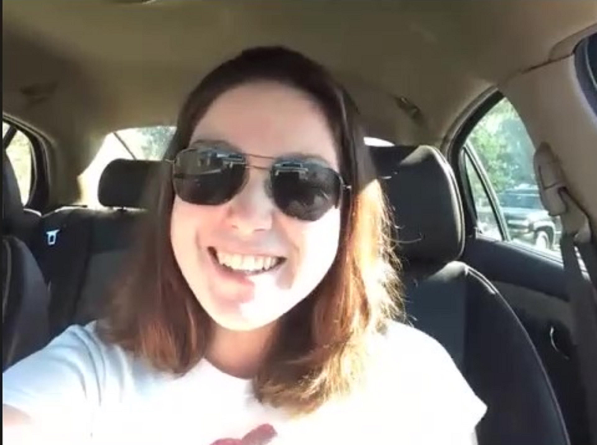a White woman wearing sunglasses smiling in a car