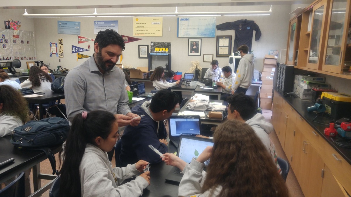 a teacher stops by a group of students in his classroom working on computers 