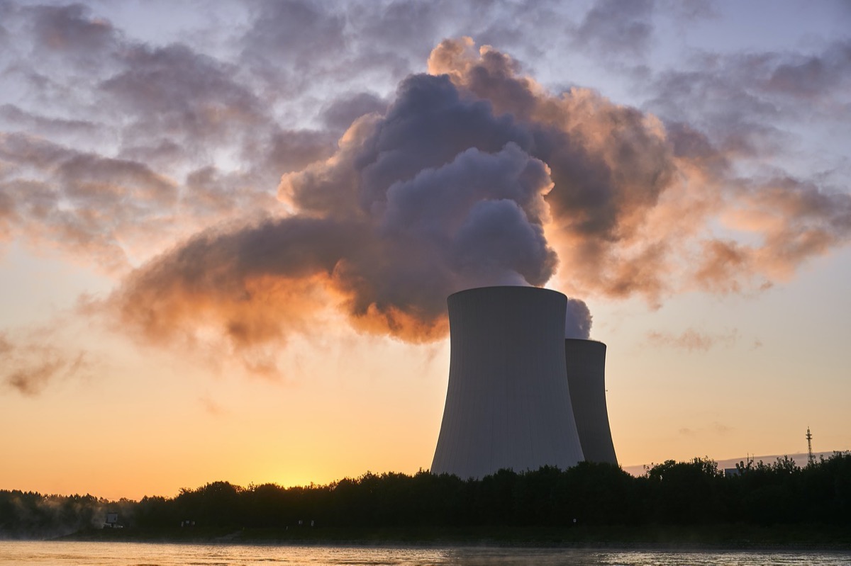 two cooling towers of a nuclear plant with steam coming out of them. the sun it setting behind them