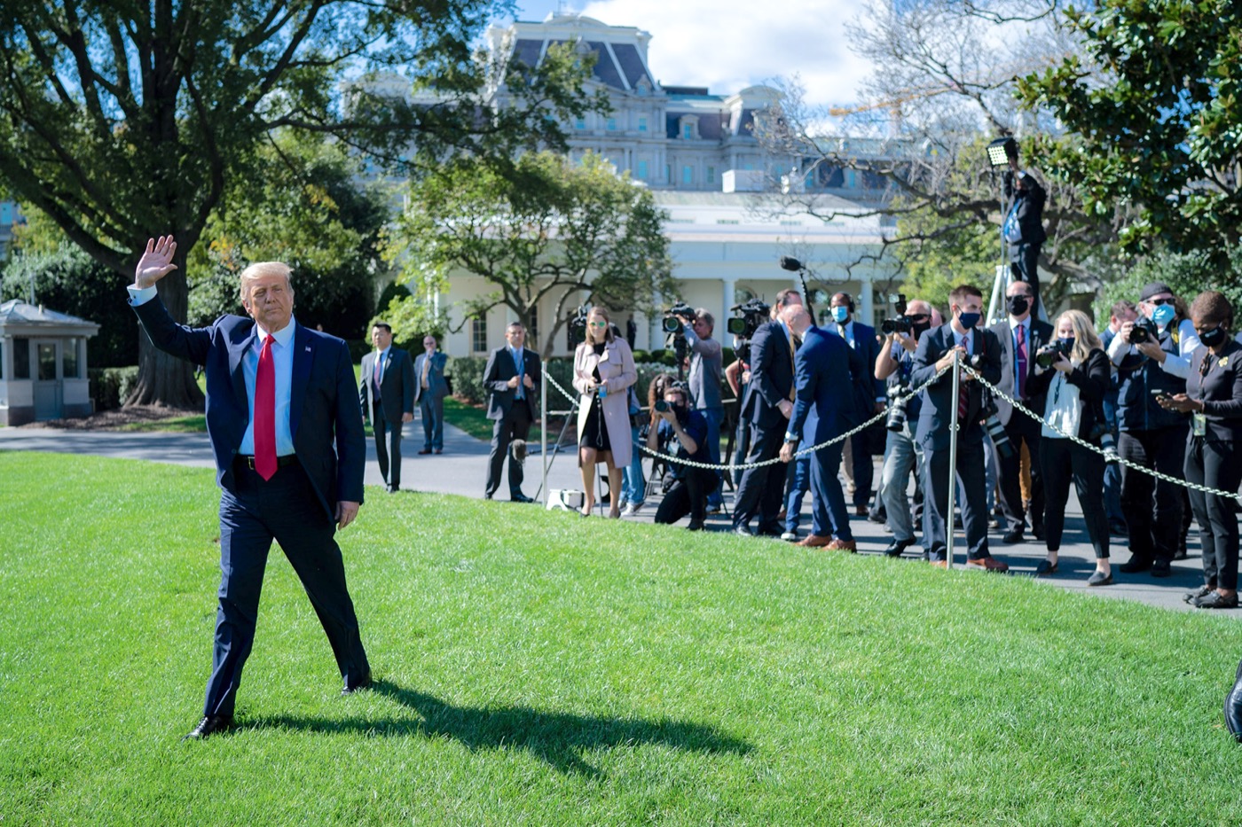 trump walking on a lawn, waving at people and press