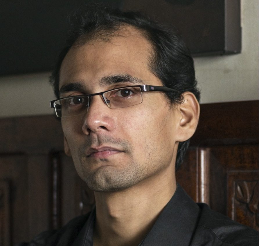 a portrait of a indian man with glasses in a black shirt