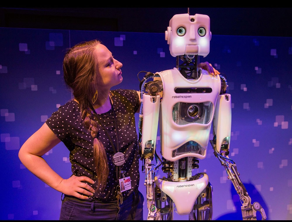 a White woman standing next to a tall humanoid robot