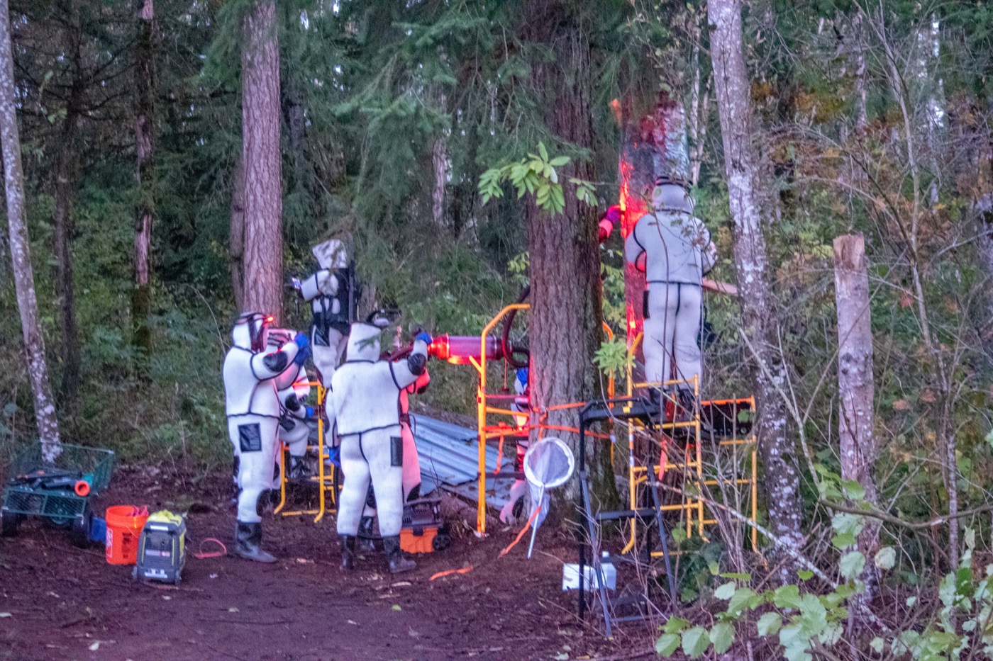 a group of people in futuristic protective gear in a forest surrounding a tree with equipment