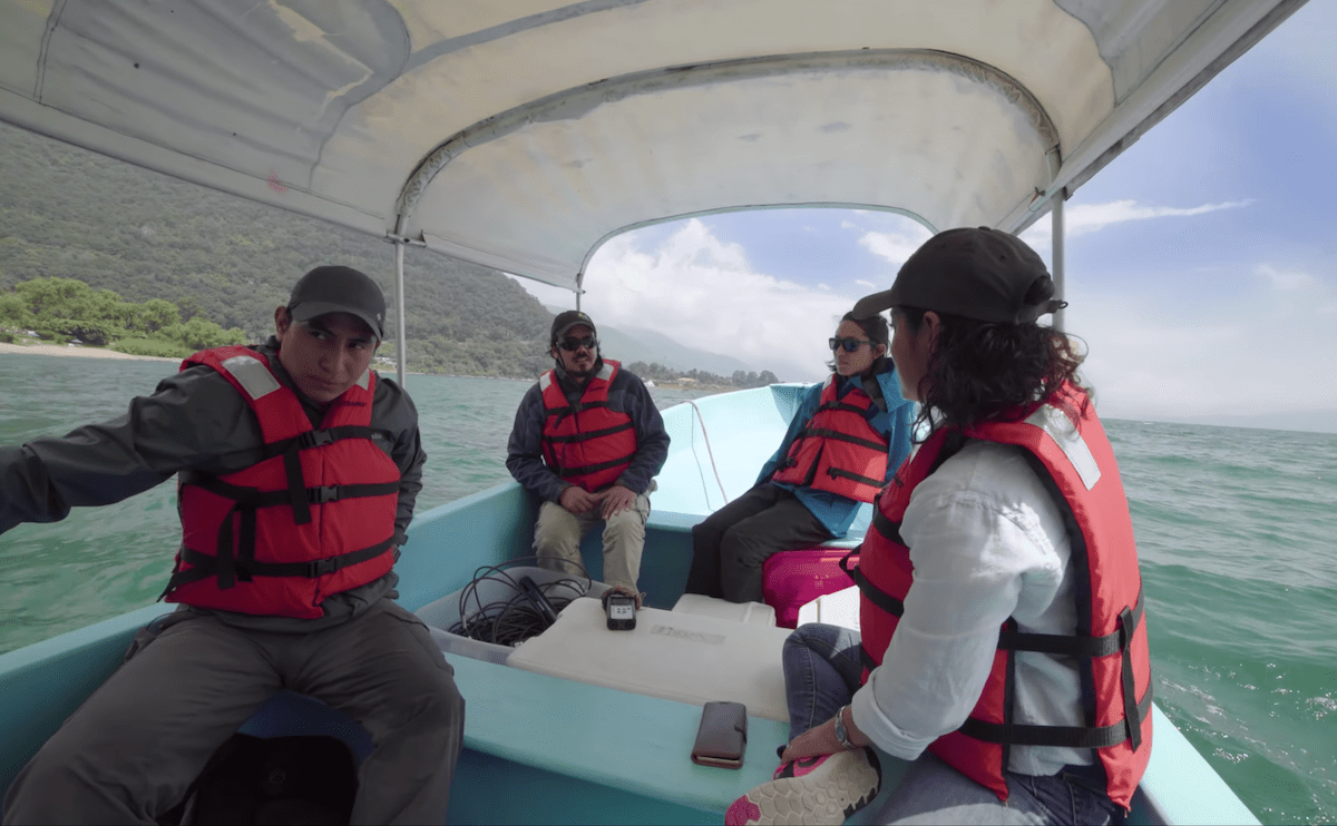 four researchers in a boat wearing life vests. they are sailing on a lake