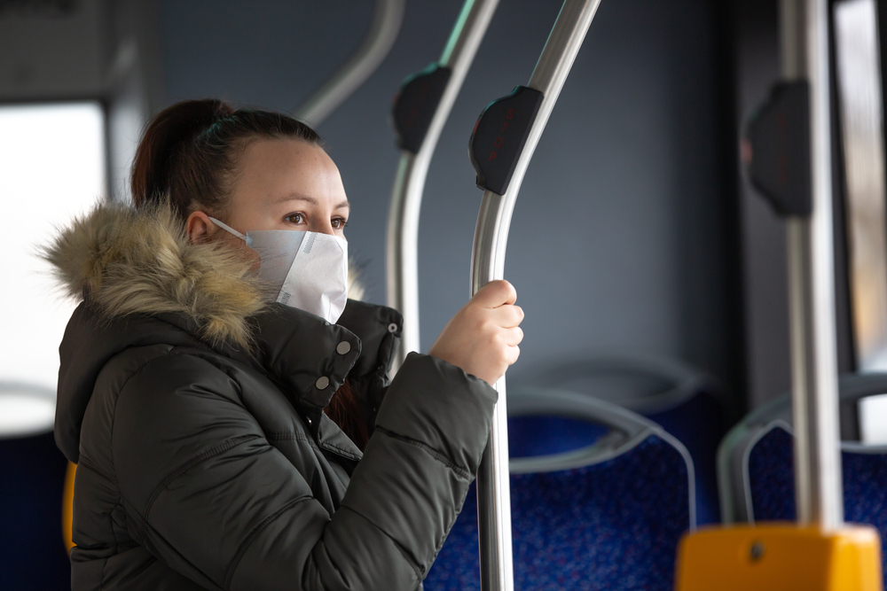 White woman wearing mask on bus holding on a pole