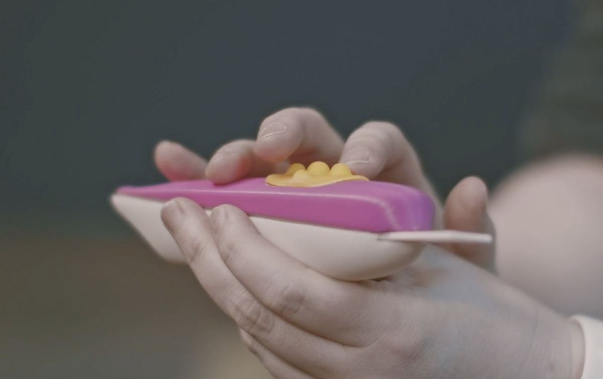 a person holds a bright pink pregnancy test stick that is larger and has a longer broader tip and textured surfaces that are easy to find and feel