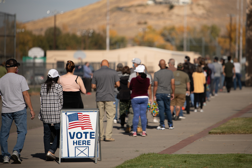 a long line of voters outside with "vote here" sign