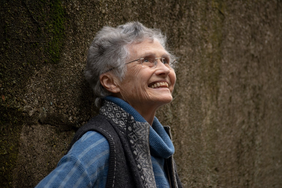 a headshot of a woman with short gray hair and glasses smiling and looking upward
