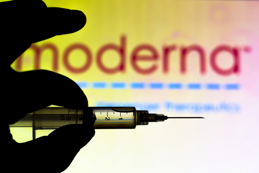 a hand holding up a syringe with the word 'moderna' in the background