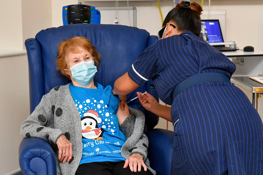 woman nurse giving older woman a vaccine shot, both wearing masks