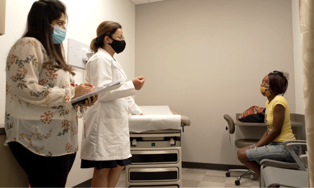 a female doctor and a female nurse wearing face masks debrief with a black woman patient in a face mask in a doctor's office