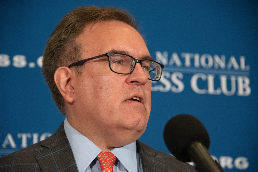 a White man in a suit in front of a microphone with a wall that says "national press club" behind him