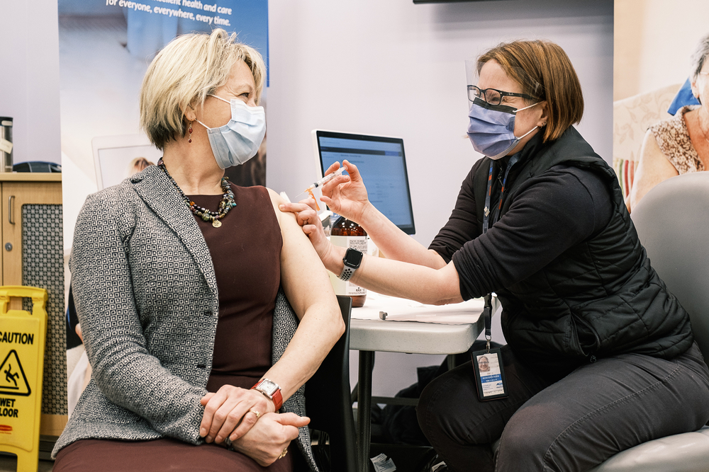 White woman giving another white woman a vaccination, both wearing masks