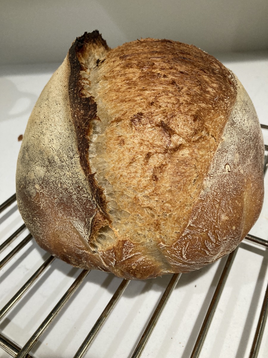 a round loaf of baked sourdough bread on a cooling rack