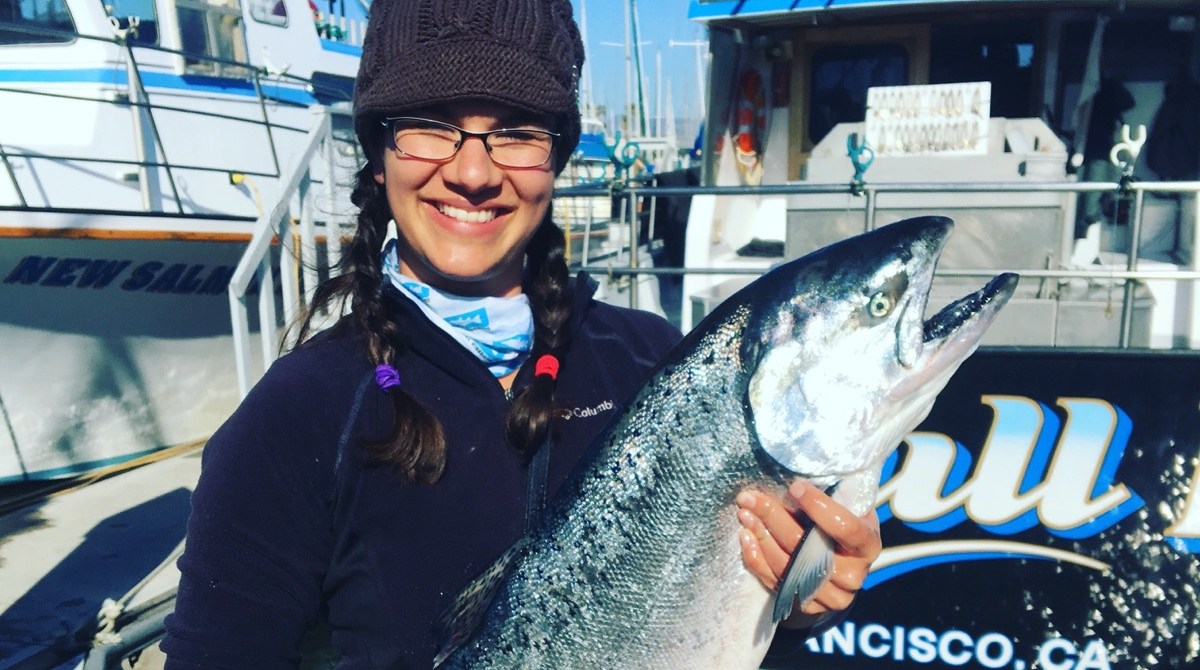 a woman in glasses and a beanie holds a large fish