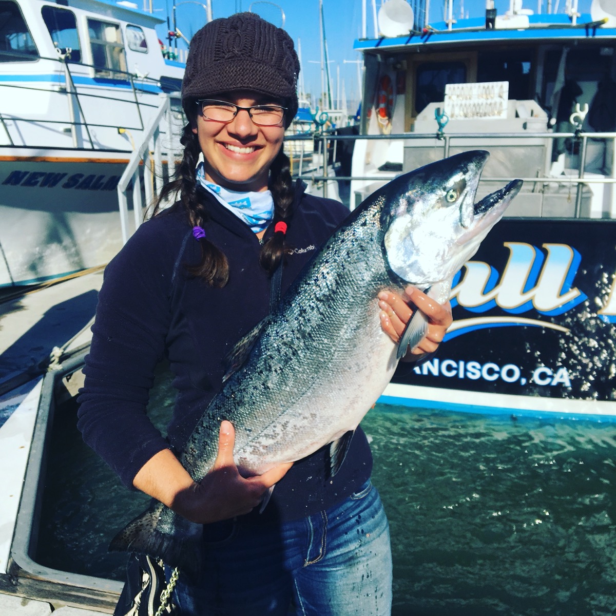 a woman in glasses and a beanie holds a large fish