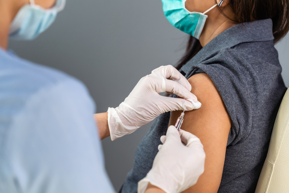 a nurse administering a vaccine to a woman, both wearing masks