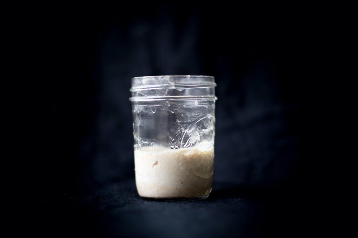 a mason jar with a white liquid, which is a sourdough starter, on a black backdrop
