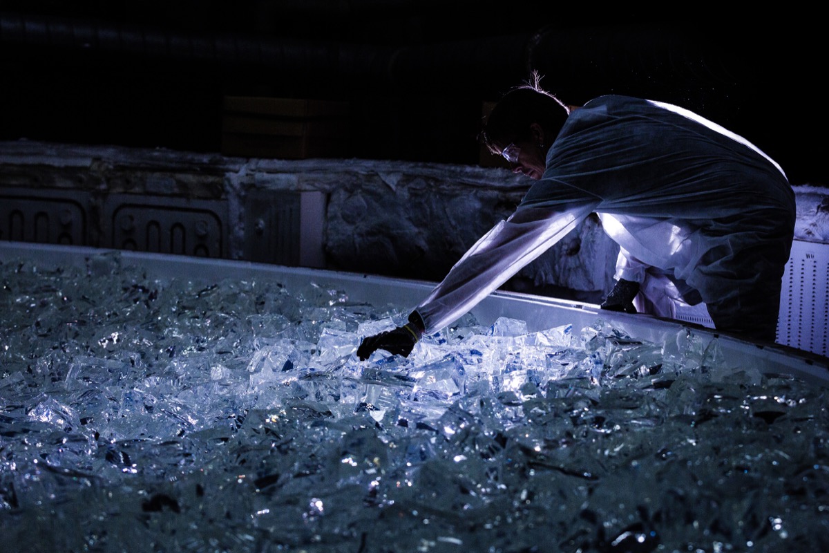 eerie-looking photo of a worker in the dark arranging large chunks of glass on a huge plate. the worker is reaching their arm out