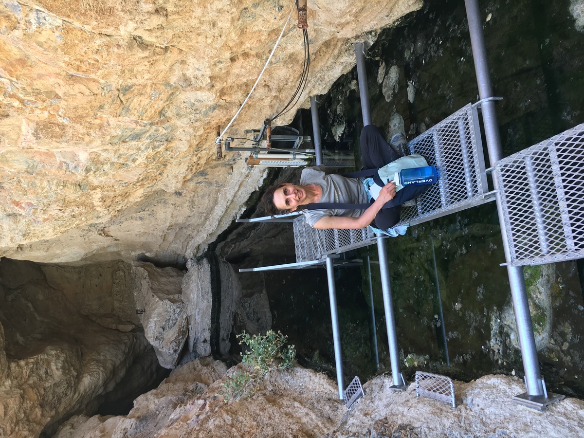 a woman sitting on narrow metal grated platforms over a waterway cutting through rock walls surrounding her