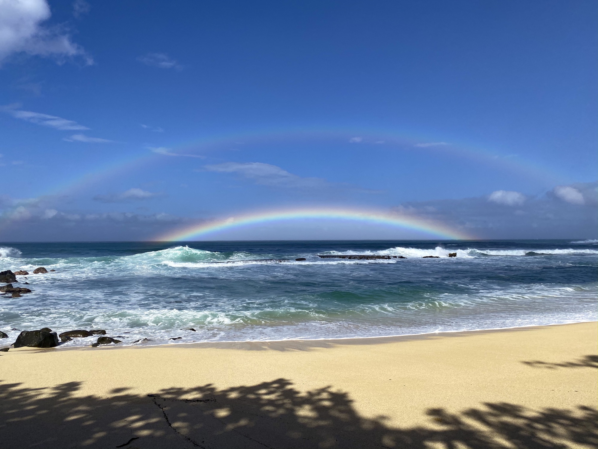 a double rainbow, the primary bow hanging low in the horizon over a beach